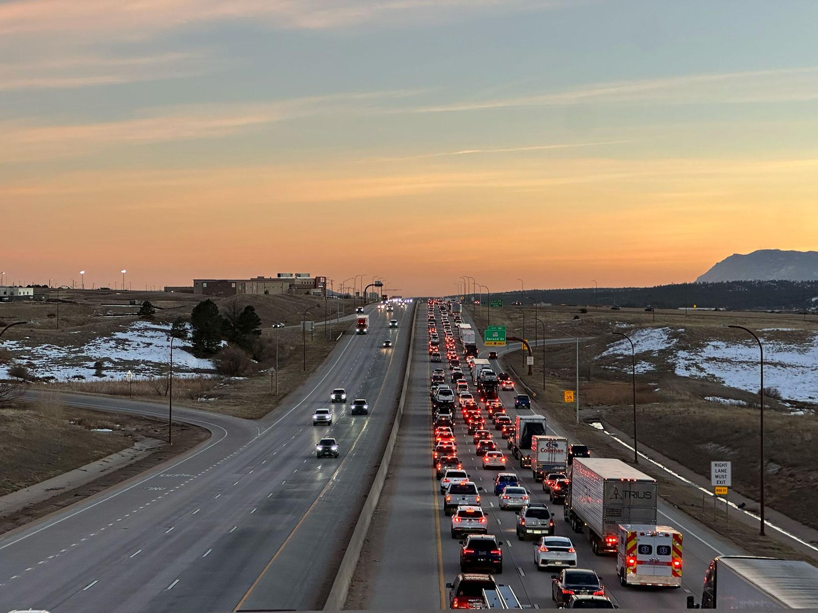 Traffic queued on Interstate 25 near Monument at sunset, with snow beside the highway.